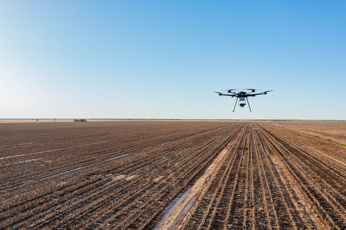 A drone flies over a dry, harvested field