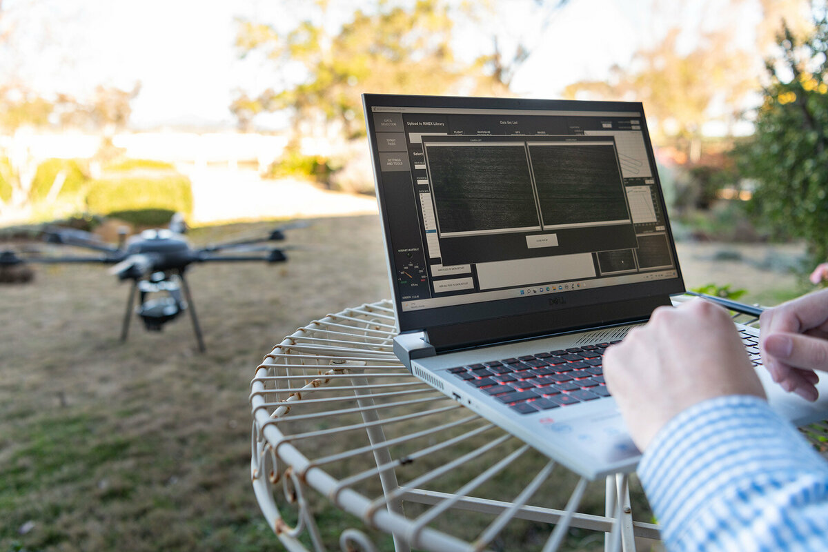 A person is using the WeedMapper program on their computer. In the background is a drone sitting on the grass